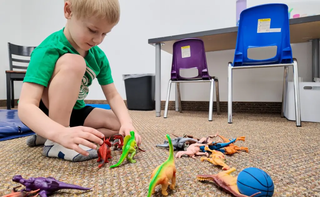 A child sitting on the carpet playing with plastic dinosaurs