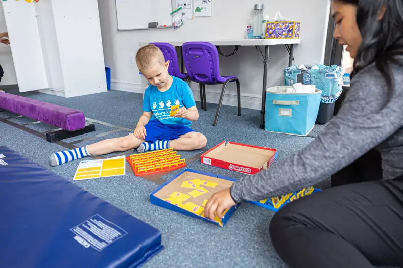 A boy playing a board game with a therapist in the playroom