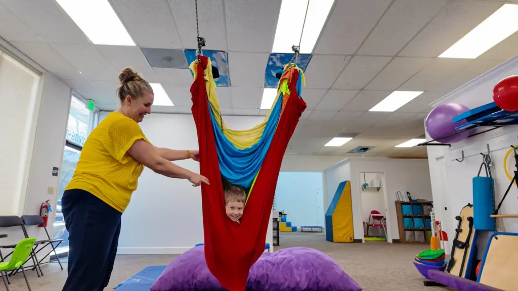 A boy smiling while swinging in colorful hammocks during physical therapy